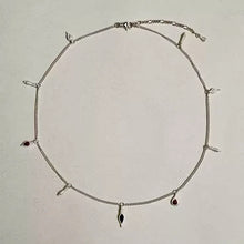 delicate silver chain necklace with black and red teardrop charms on beige background