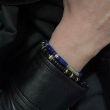 Close-up of wrist wearing black, blue, and silver beaded bracelets against a black leather jacket