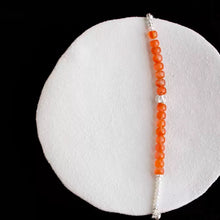 Orange and white beaded bracelet with silver clasp on textured white round surface and black background