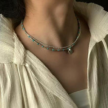 Close-up of a woman's neck wearing layered beaded necklaces with turquoise and silver beads, paired with a textured cream blouse