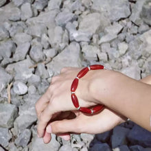 Hand wearing red bead bracelet with silver spacers on rocky ground background