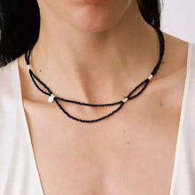 Woman wearing a double-layered black beaded necklace with white accents on bare neck and white top
