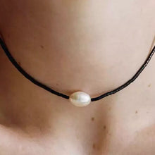 Close-up of a black beaded necklace with a single white pearl pendant on neck