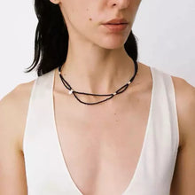 Woman wearing minimal black beaded layered necklace with silver accents, dressed in white sleeveless top