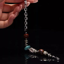 Hand holding a silver chain bracelet with turquoise and red beads on black background