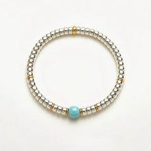 Silver beaded bracelet with a central turquoise bead and small gold spacer beads