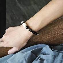 Close-up of wrist wearing black and white bead bracelet on wooden surface with blue fabric