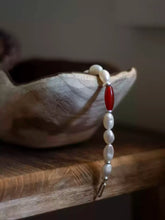 White pearl and red bead bracelet draped over edge of textured wooden bowl on wooden surface