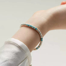 Close-up of a wrist wearing a silver and turquoise beaded bracelet on a light background