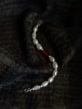 Pearl bracelet with irregular white pearls and a single brown bead on textured black fabric