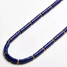 Close-up of blue cylindrical beads necklace with small gold spacer beads on white background