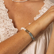 Woman wearing lace-trimmed white top, pearl necklace, and blue stone and pearl bracelet on arm