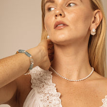 Close-up of woman wearing pearl necklace, pearl earrings, and aquamarine stone bracelet with lace top