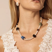 Close-up of woman wearing gemstone and pearl beaded necklace with white lace top and pearl earrings