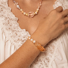 close-up of woman's arm wearing an orange gemstone and pearl bracelet with a matching beaded necklace and white lace top
