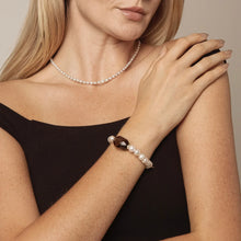 Woman in black off-shoulder top wearing pearl necklace and pearl bracelet with brown stone