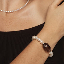 Pearl necklace and pearl bracelet with a large dark gemstone worn on arm over black top