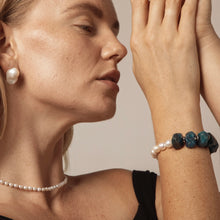 Woman wearing pearl necklace, irregular pearl earrings, and pearl and blue stone bracelet on wrist