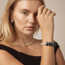 Close-up of woman wearing a pearl necklace, pearl earring, and blue gemstone bracelet with black top