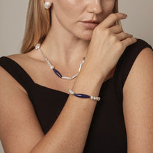 Woman wearing pearl and blue gemstone necklace, matching bracelet, and pearl earrings with black sleeveless top