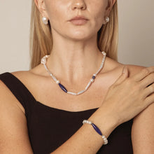 Close-up of woman wearing pearl necklace and bracelet with dark blue stone accents and black sleeveless top