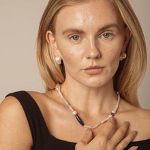 Blonde woman wearing baroque pearl earrings and necklace with blue gemstone accents in studio
