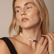 Close-up of woman wearing a pearl and blue stone choker necklace with black strap top