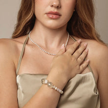 Woman wearing a pearl necklace and beaded bracelet with large clear stones, in a satin beige halter dress