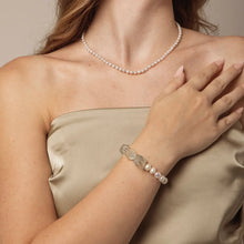 Woman wearing a pearl necklace and a bracelet with pearls and clear gemstones on beige satin dress
