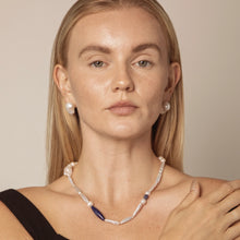 Close-up of woman with pearl earrings and necklace featuring white and blue beads on neutral background