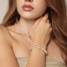 Close-up of woman wearing natural pearl necklace and clear geometric bead bracelet, beige strapless top
