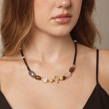 Close-up of woman wearing a gemstone bead necklace with black, brown, and clear beads on bare shoulders