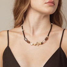 Close-up of woman wearing a beaded statement necklace with black, clear, and brown beads, and small pearls