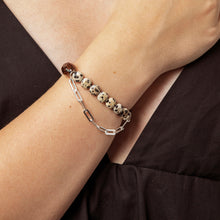 Close-up of wrist with two bracelets, one silver chain and one beige and black spotted beaded bracelet
