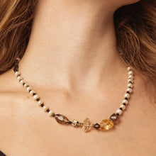 Close-up of a beaded necklace with pearls and mixed brown and amber stones on a woman's neck