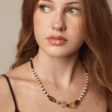 Close-up of woman with brown hair wearing a beaded pearl and gemstone necklace