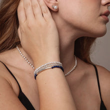 Woman wearing pearl necklace, pearl and blue gemstone bracelets, and pearl stud earrings in black top
