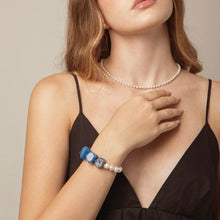 Woman in black dress wearing a pearl necklace and blue gemstone pearl bracelet with natural lighting