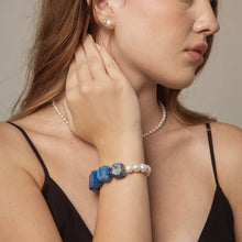 Woman wearing pearl necklace, pearl and blue gemstone bracelet, and pearl stud earrings in black strap dress