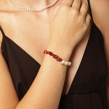 Close-up of a woman's arm wearing a red coral and white pearl bracelet with a matching pearl necklace and black dress