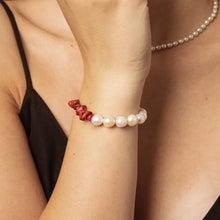 Close-up of wrist wearing a bracelet with white pearls and red coral beads on a woman in a black top