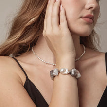 Close-up of woman wearing a black strap top with a pearl necklace and a chunky pearl and stone bracelet