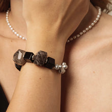 Close-up of wrist wearing bracelet with large smoky quartz and black beads, model also wears pearl necklace