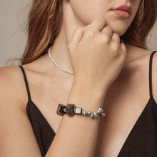 Close-up of woman wearing black top with beaded bracelet and pearl necklace, minimal jewelry fashion