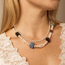 Close-up of woman wearing layered pearl necklaces with blue, black, clear, and green stone beads
