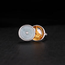 Silver ring with a jade cover and golden Buddha statue inside on black surface
