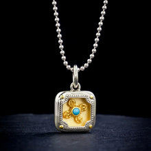 silver pendant necklace with gold decorative cross and turquoise center on black background