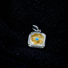 Square pendant with gold flower and blue stone center, silver frame on black velvet