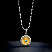 Silver pendant necklace with round yellow and blue center design on black background