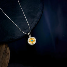 Silver necklace with round gold and turquoise pendant on dark textured background